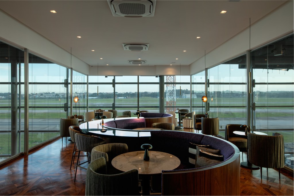Vista panorâmica do Nubank Ultravioleta Lounge com janelas para a pista
